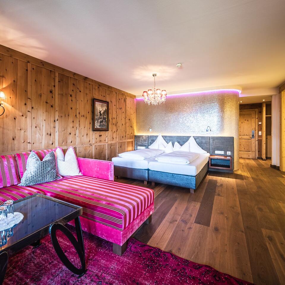Hotel room with double bed, pink sofa and wood paneling