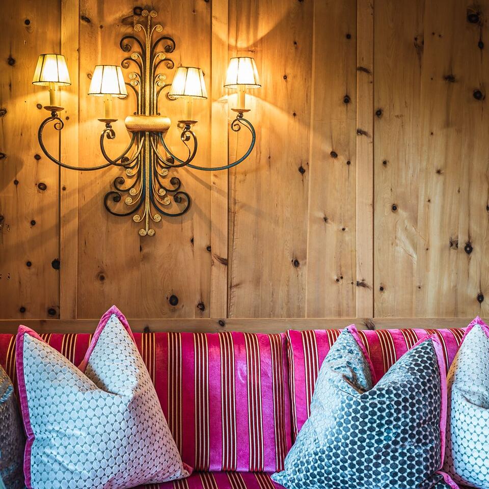 Wall lamp above pink striped bench with cushions in front of wooden wall
