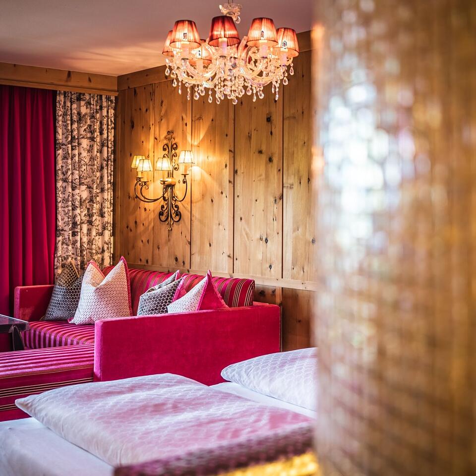 Hotel room with red sofa, bed, wooden wall, chandelier and wall lamp