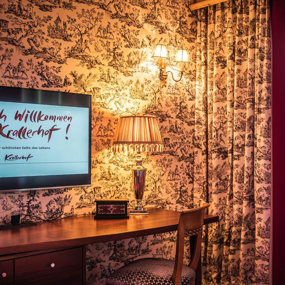 Hotel room with desk, lamp, TV and patterned wallpaper