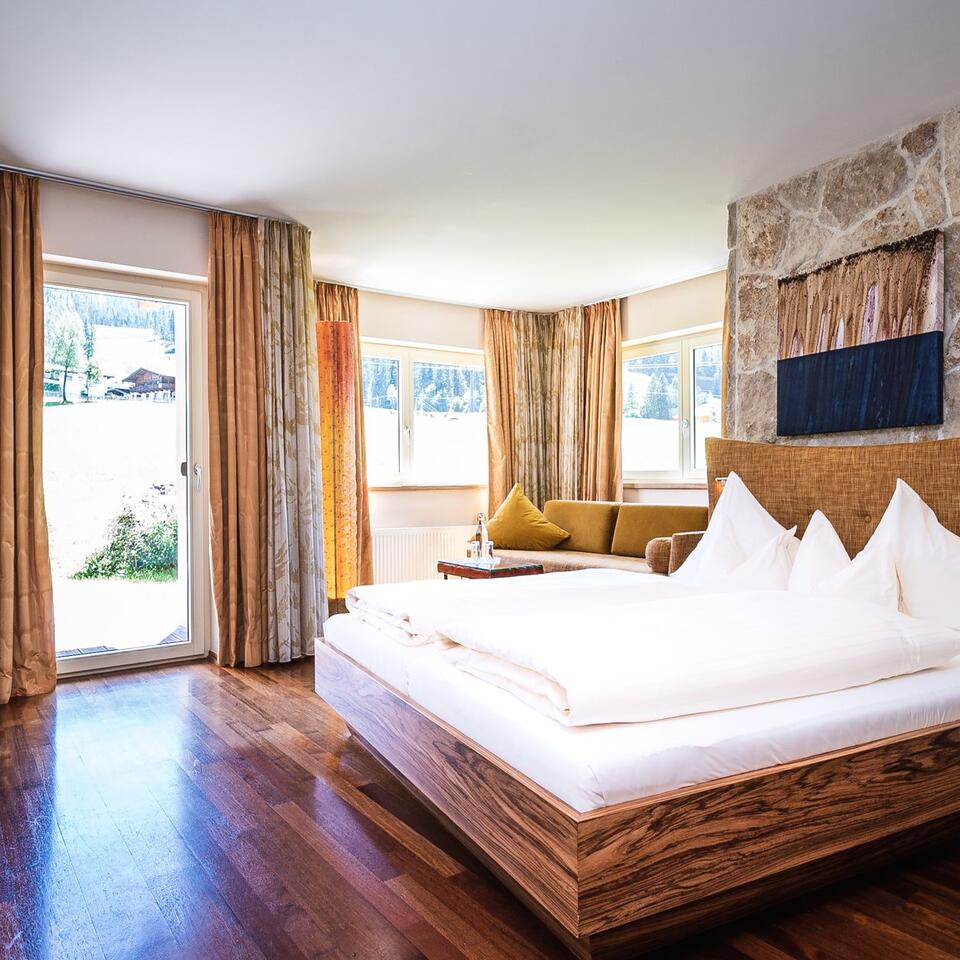 Helles Hotelzimmer mit Doppelbett, Sofa und Blick in die Natur