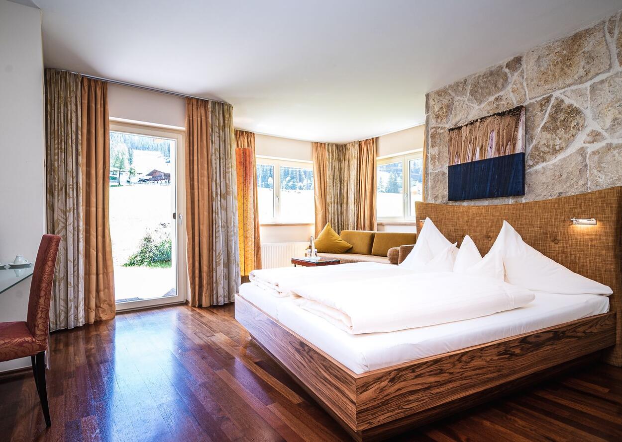 Helles Hotelzimmer mit Doppelbett, Sofa und Blick in die Natur