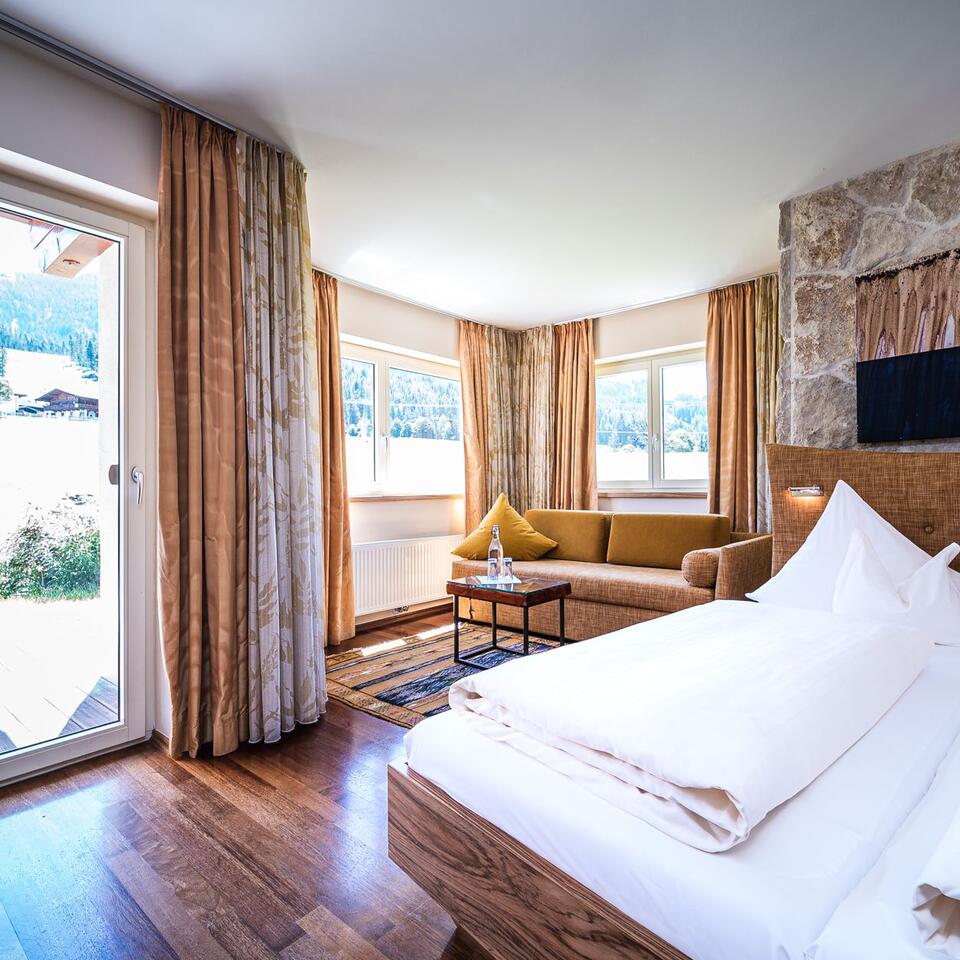 Helles Hotelzimmer mit Doppelbett, Sofa, Fenster und Tür zur Natur
