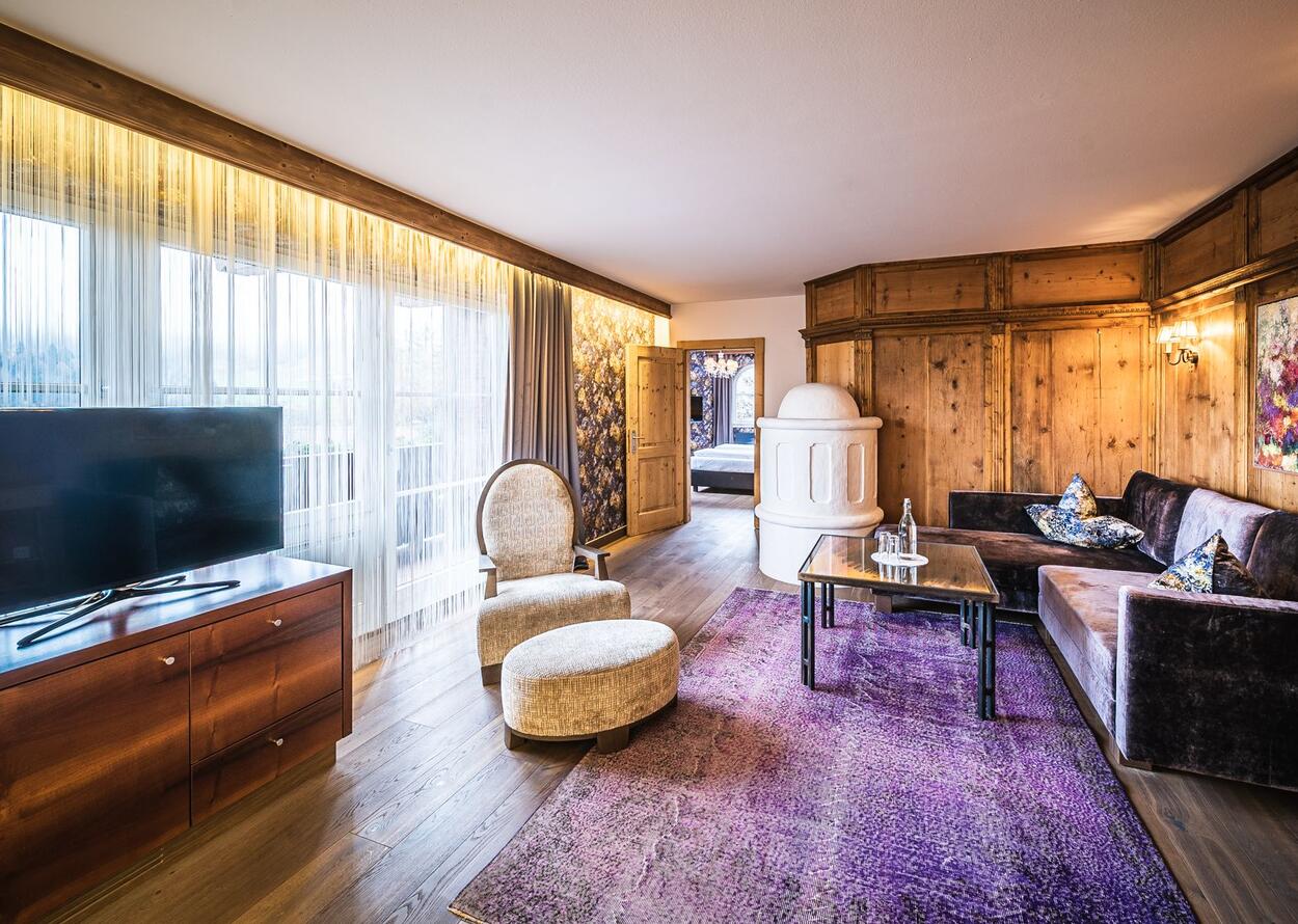 Hotelzimmer mit Sessel, Sofa, Teppich, Kaminofen und Holzwand