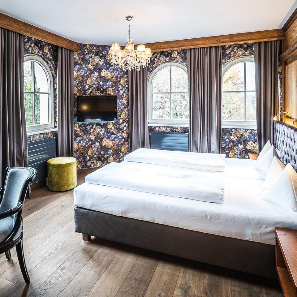 Hotel room with double bed, floral wallpaper, three windows and chandelier