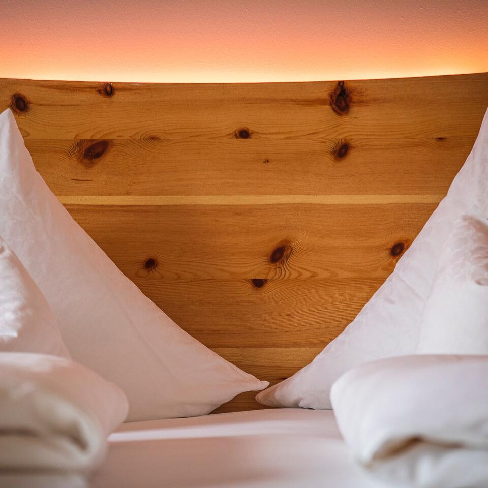 Bed with white bedding and wooden headboard in front of orange lighting