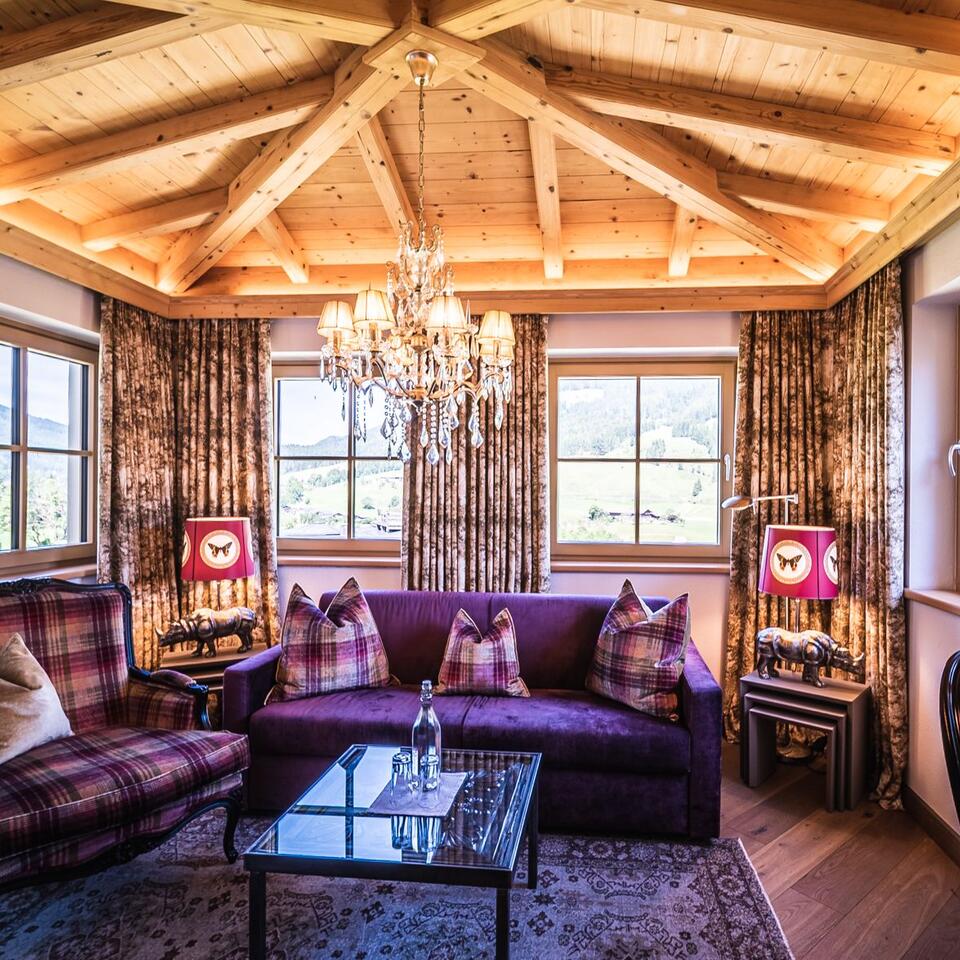 Gemütliches Wohnzimmer mit lila Sofa, kariertem Sessel, Kronleuchter und Holzdecke