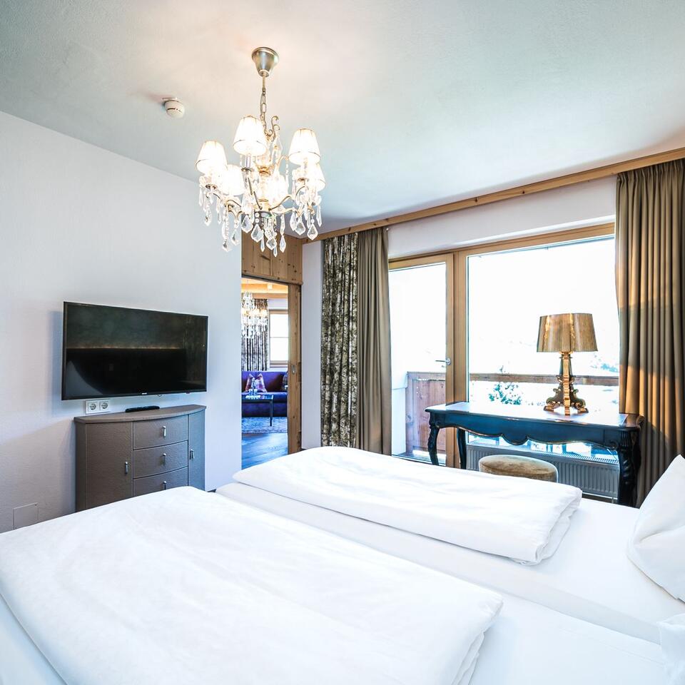 Helles Hotelzimmer mit Doppelbett, Fernseher, Kronleuchter und Balkon