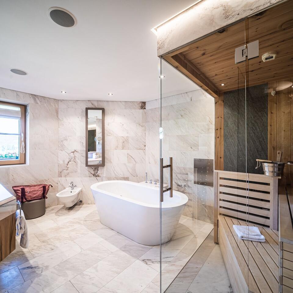 Helles Badezimmer mit freistehender Badewanne und Sauna hinter Glaswand