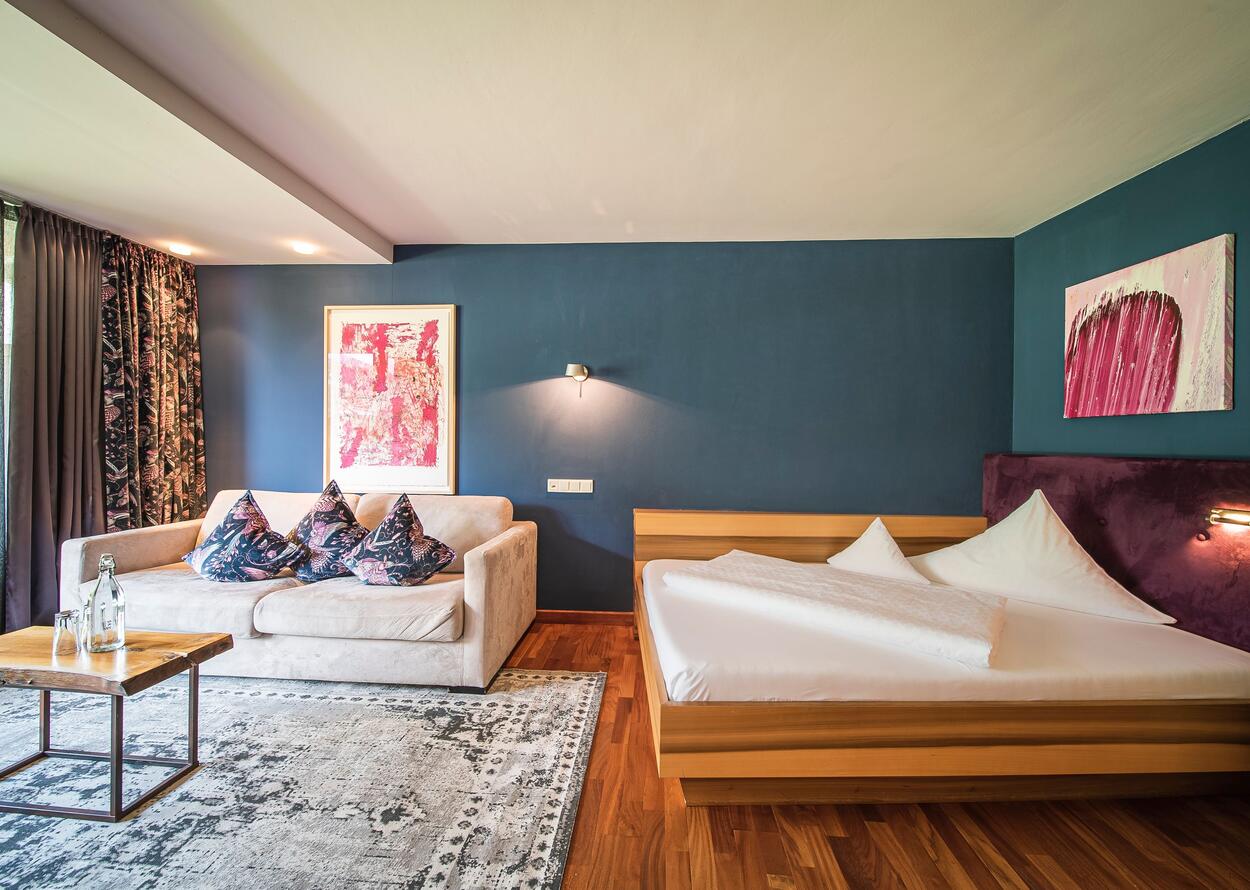 Hotelzimmer mit Doppelbett, Sofa, Teppich und blauer Wand