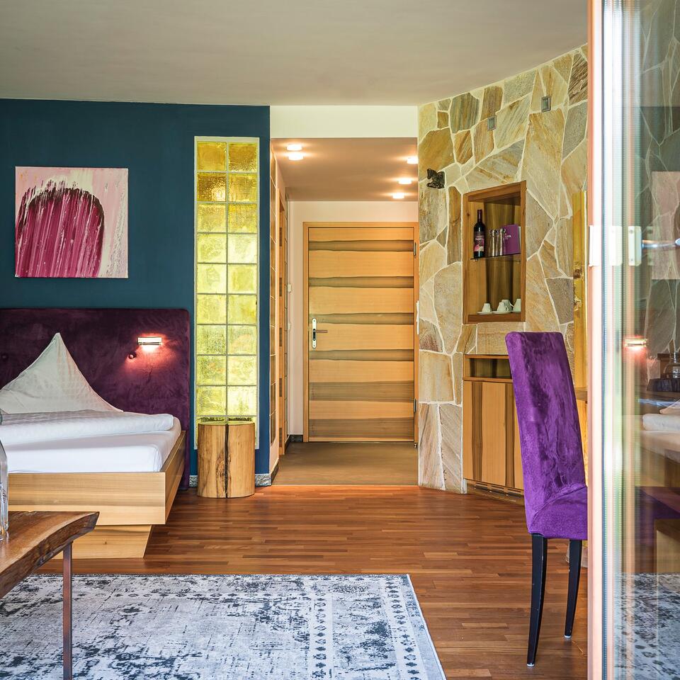 Hotel room with bed, purple accents, wooden floor and stone wall