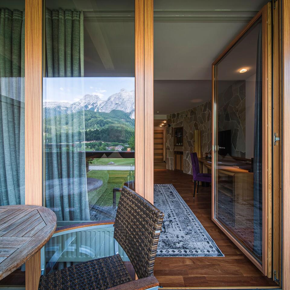 View through open balcony door to mountain landscape and interior with carpet and furniture
