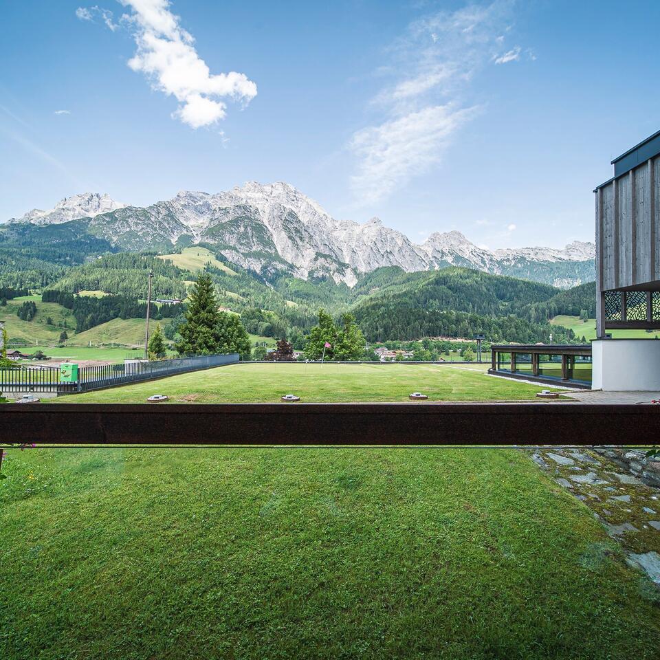 Green meadow in front of a mountain panorama with wooded slopes and blue sky