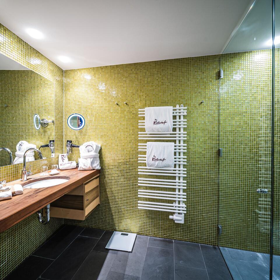 Modern bathroom with green mosaic tiles, wooden wall, sink and towel warmer