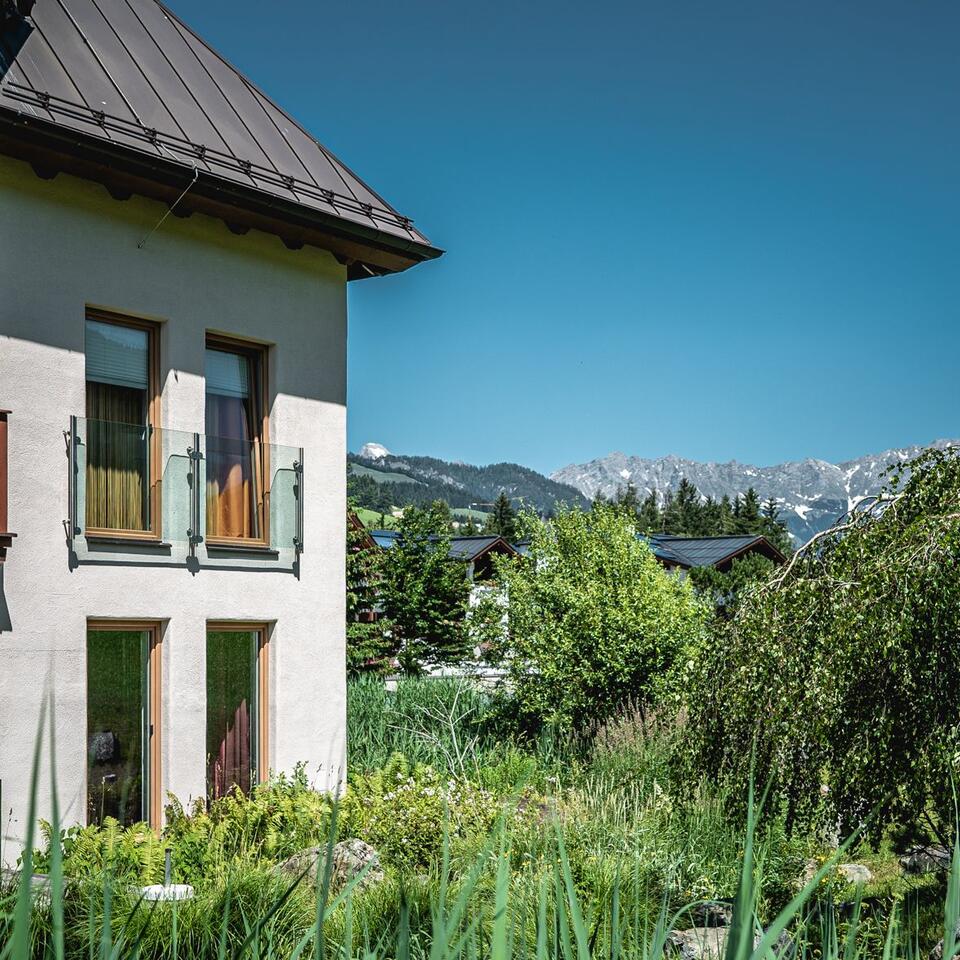 Hausfassade mit Balkon, Garten und Bergen im Hintergrund