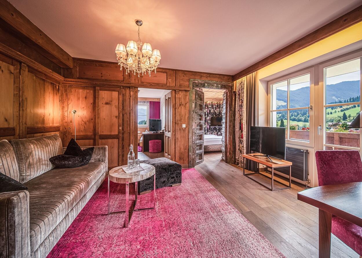 Wohnzimmer mit Holzvertäfelung, rosa Teppich und Blick in ein Schlafzimmer