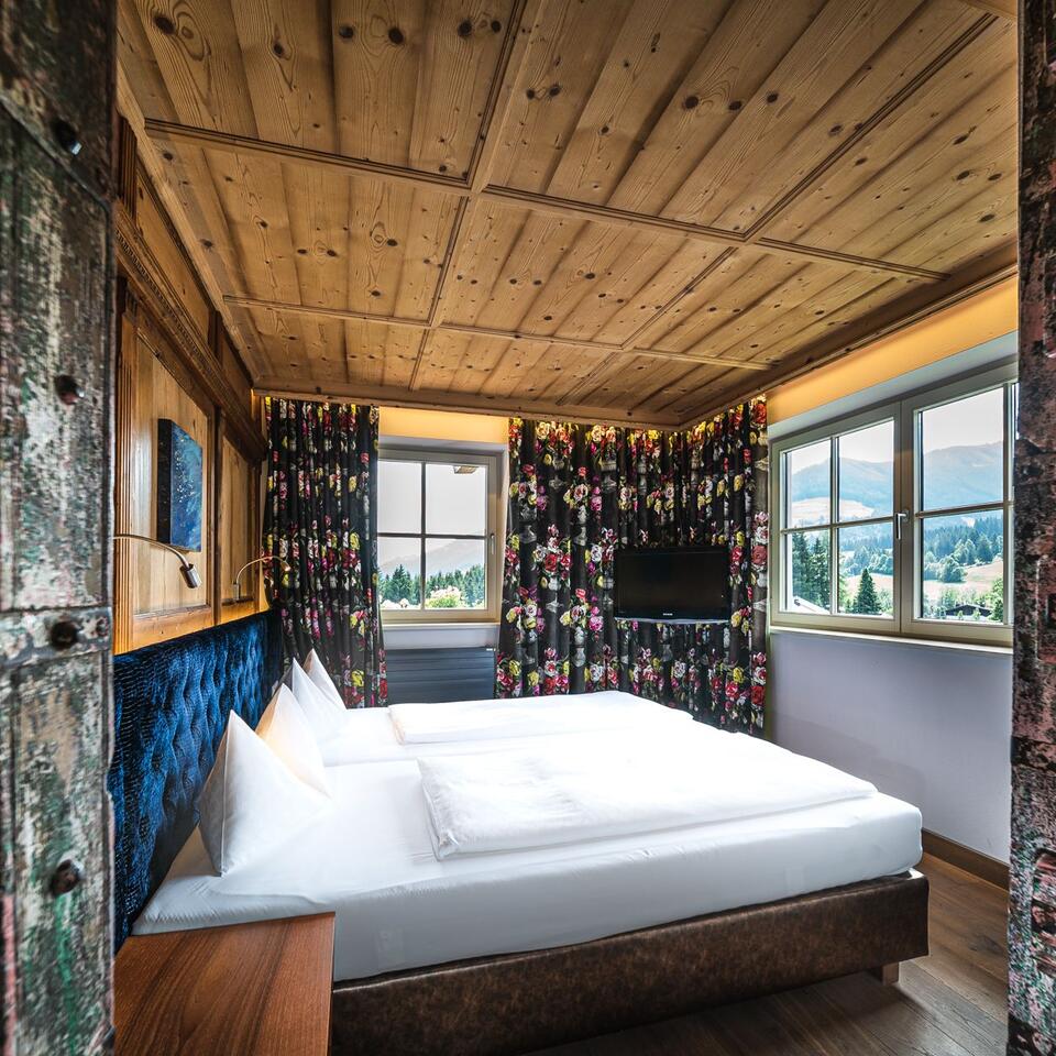 Bedroom with wooden walls, double bed, floral curtains and view of green hills