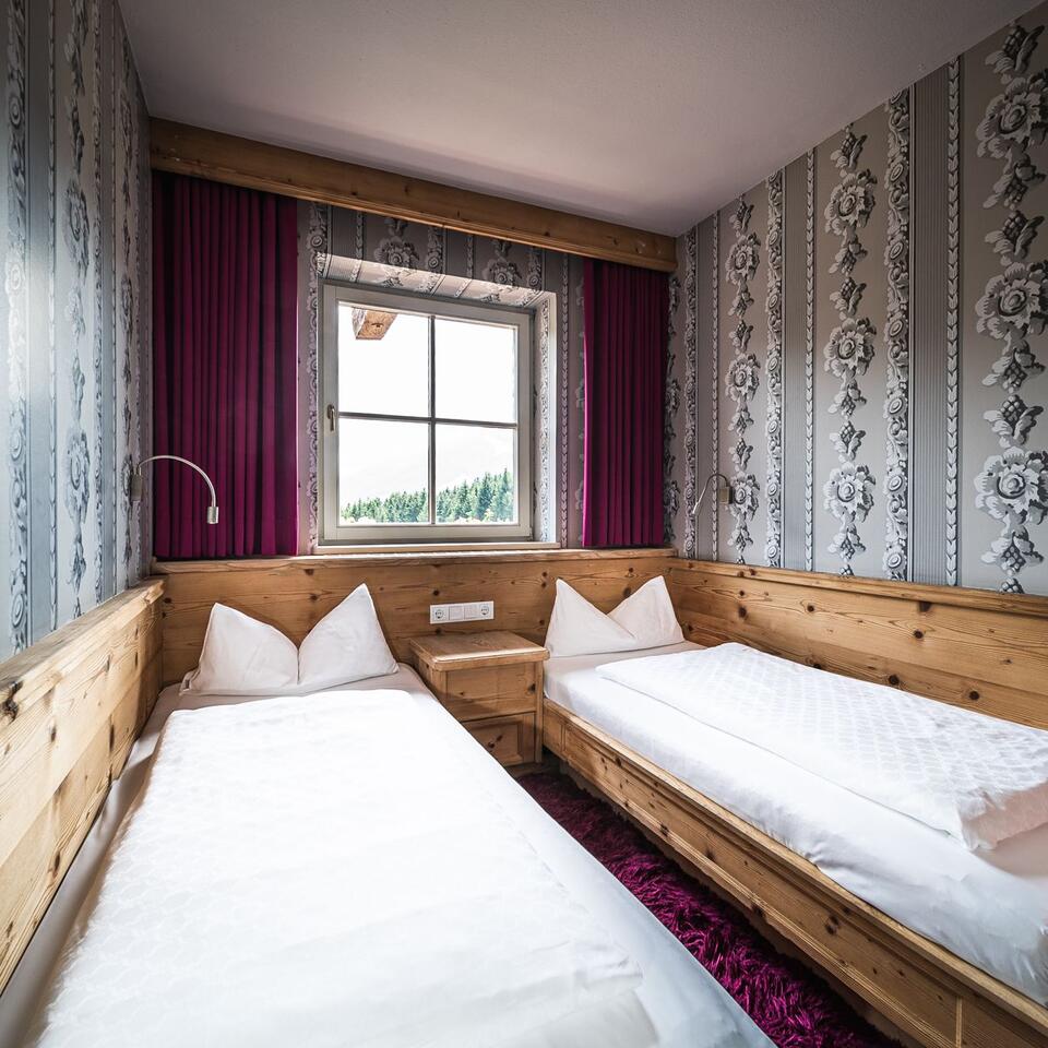 Two single beds in a room with patterned wallpaper and window