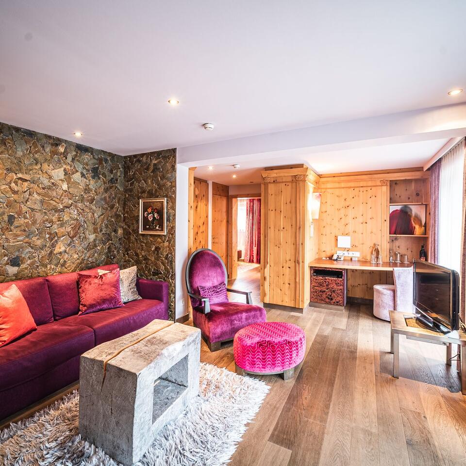 Living room with purple sofa, armchair and stool, wooden wall and stone coffee table