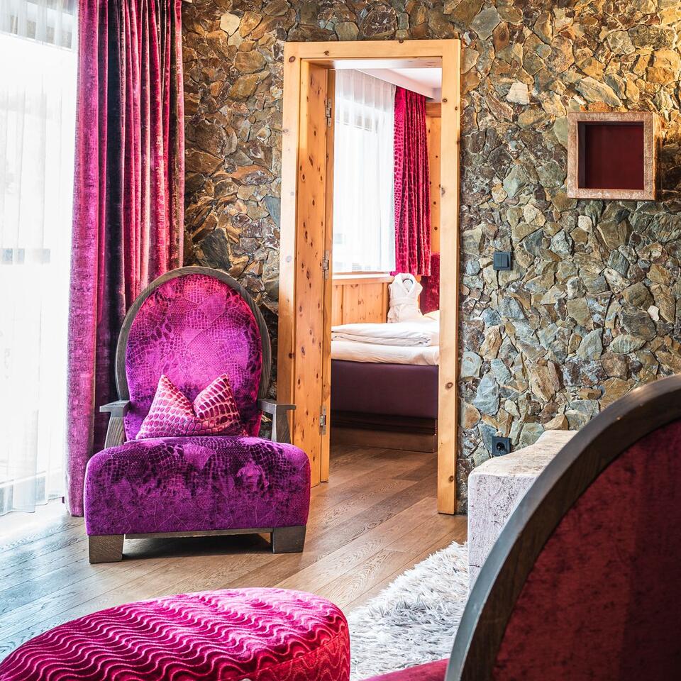 Room with purple armchair, stone wallpaper and view through a wooden door onto a bed