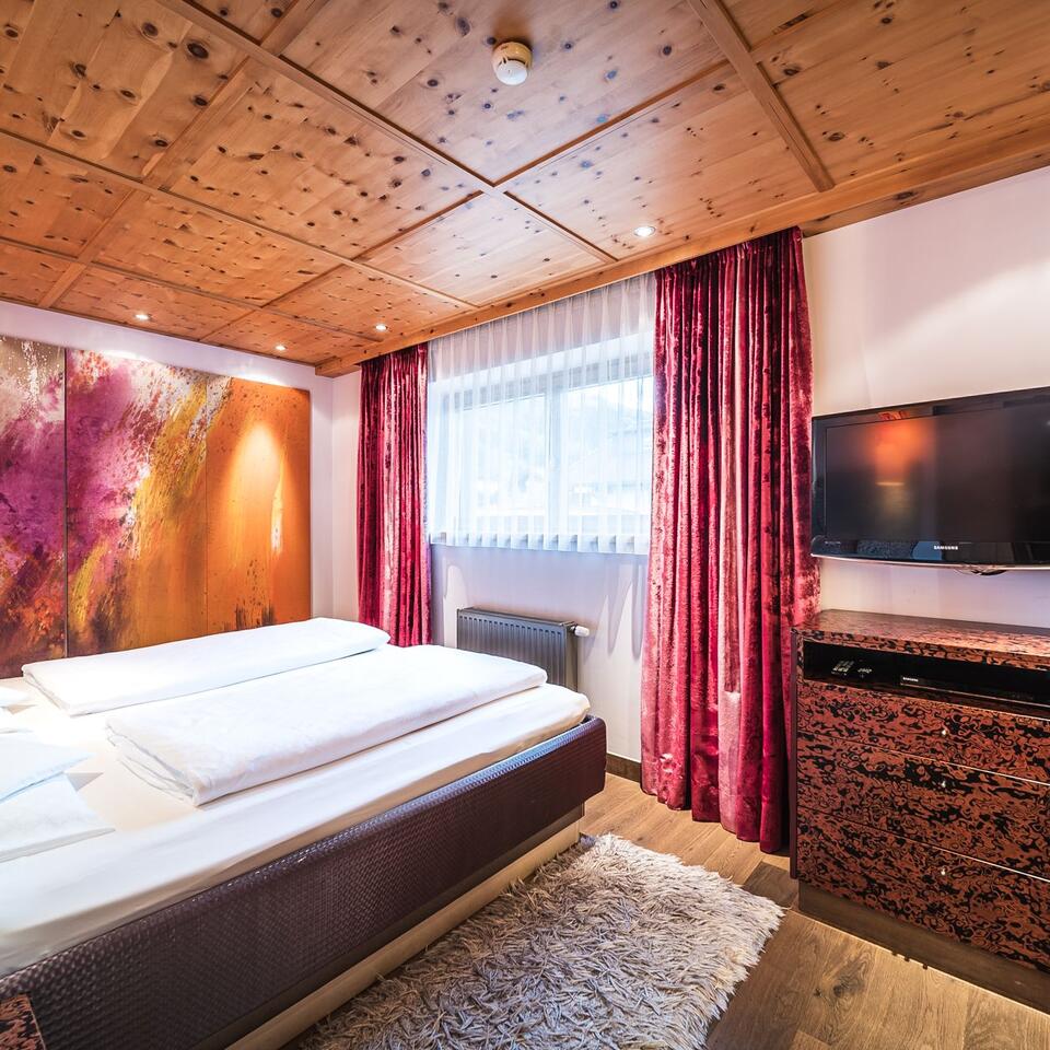 Bedroom with double bed, wooden ceiling, red curtain and abstract mural