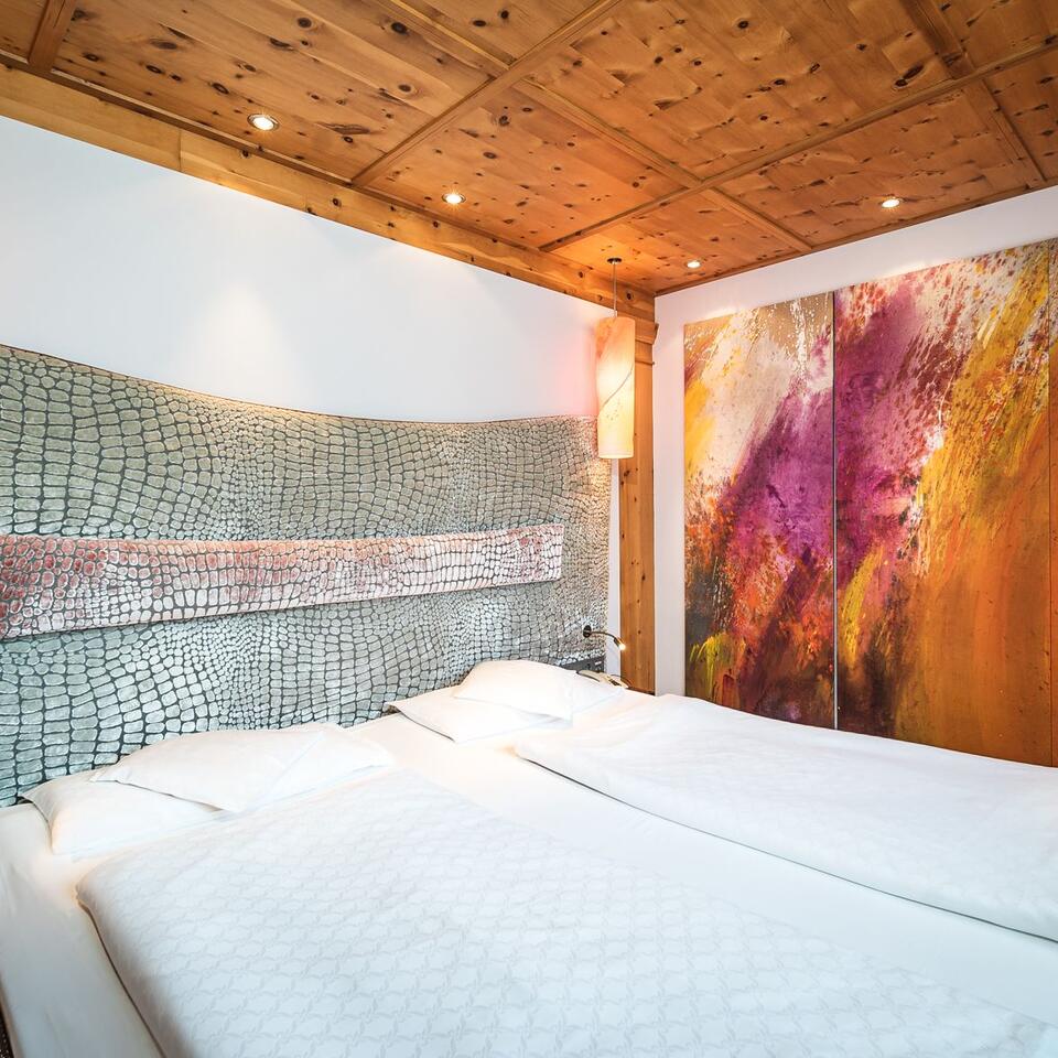 Bedroom with double bed, patterned headboard, wooden beamed ceiling and abstract painting
