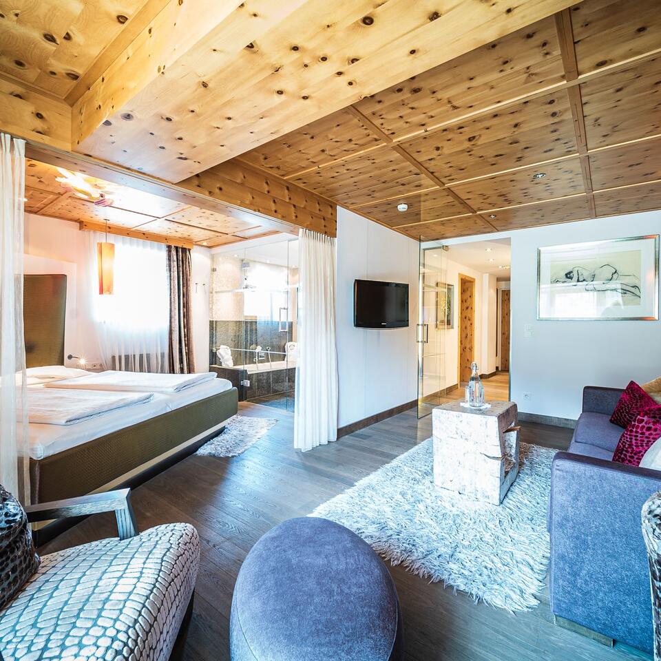 Helles Hotelzimmer mit Holzbalkendecke, Doppelbett, Sitzecke und Bad