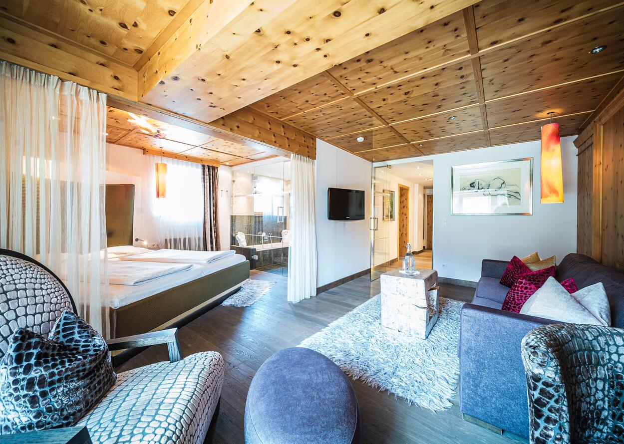 Helles Hotelzimmer mit Holzbalkendecke, Doppelbett, Sitzecke und Bad