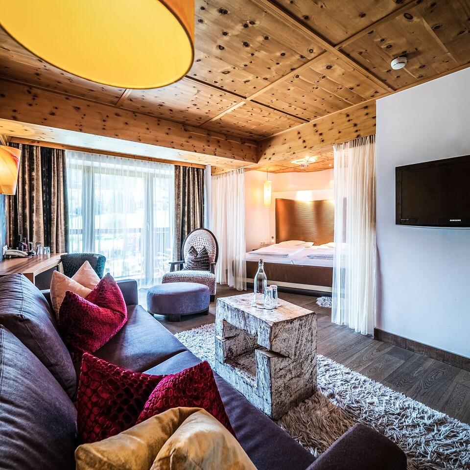 Gemütliches Hotelzimmer mit Holzbalkendecke, Sofa, Bett und Fernseher