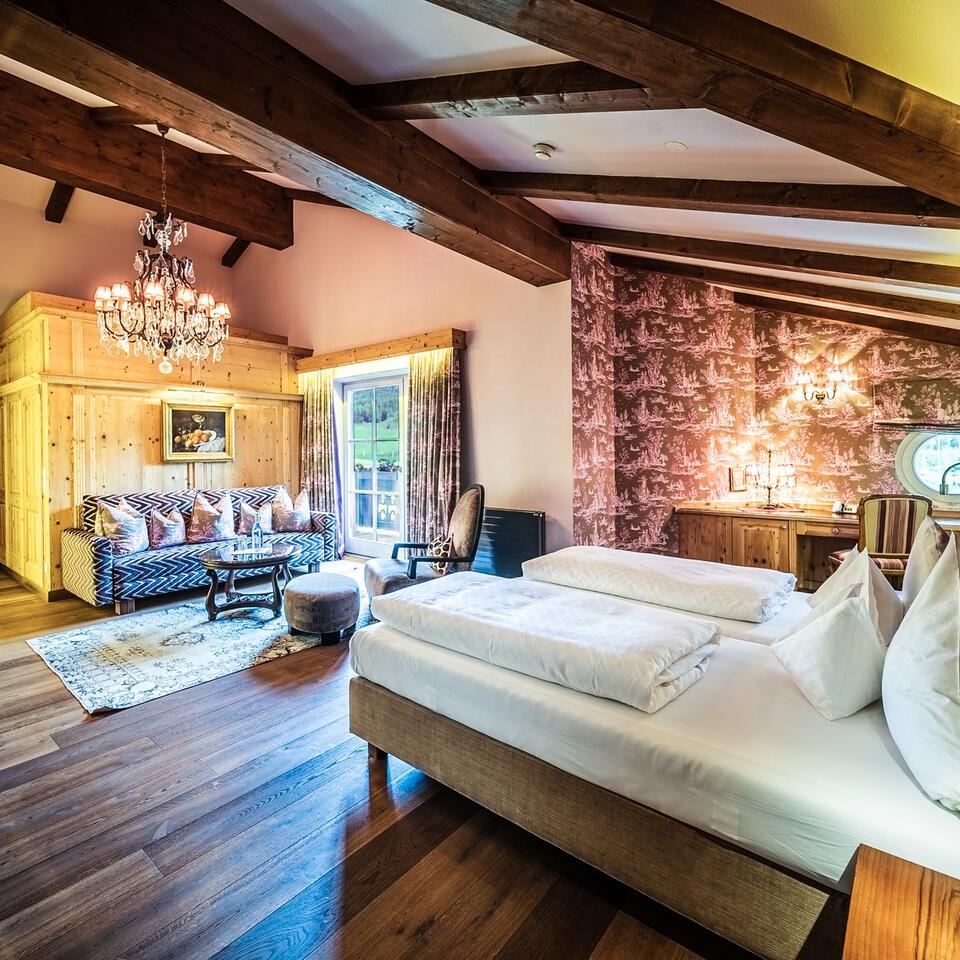 Hotelzimmer mit Doppelbett, Sofa, Kronleuchter und Holzbalkendecke
