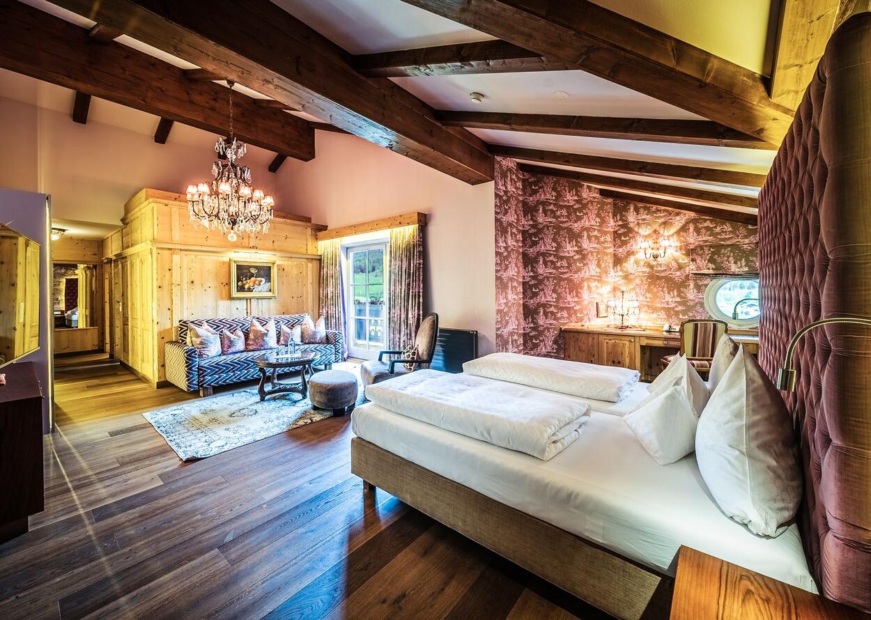 Hotelzimmer mit Doppelbett, Sofa, Kronleuchter und Holzbalkendecke