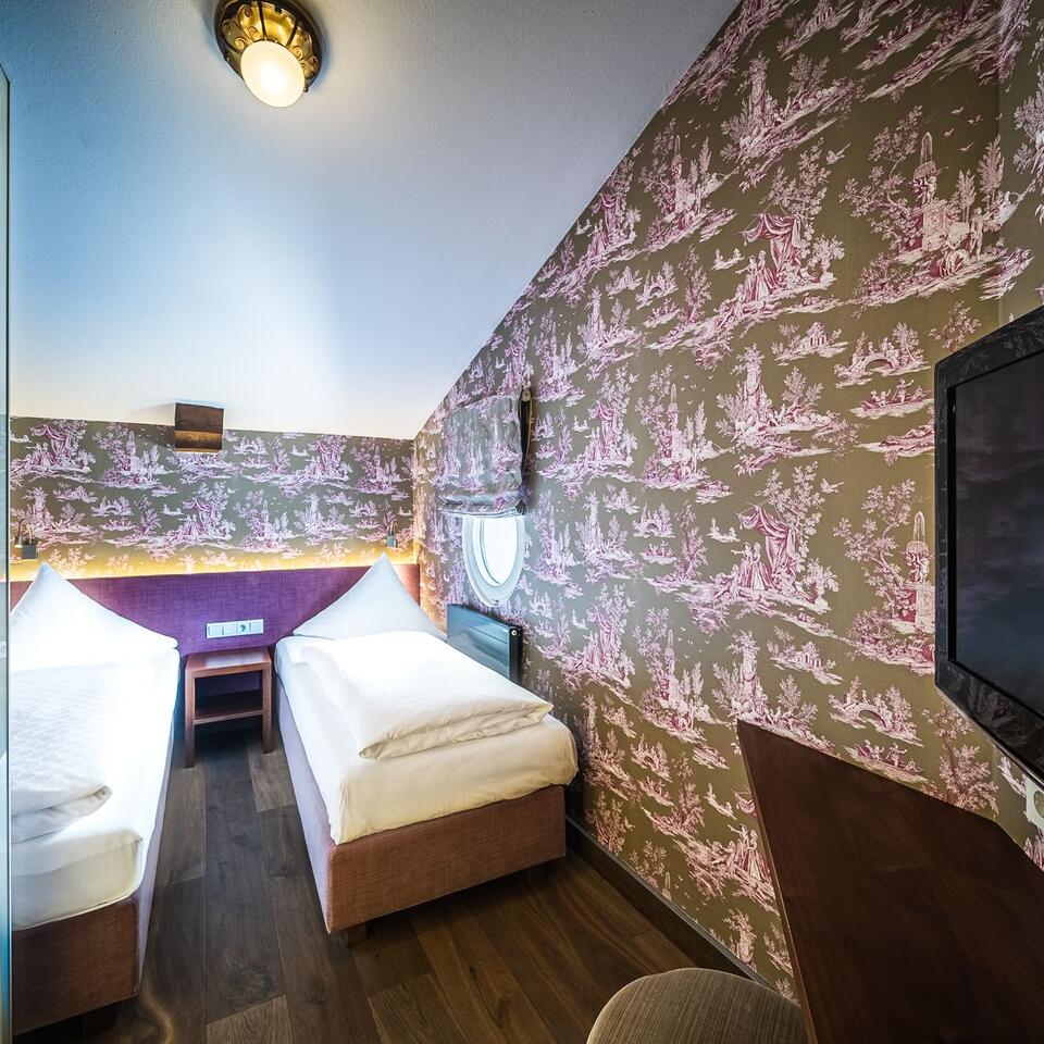 Zimmer mit zwei Betten, gemusterter Tapete und Dachschräge