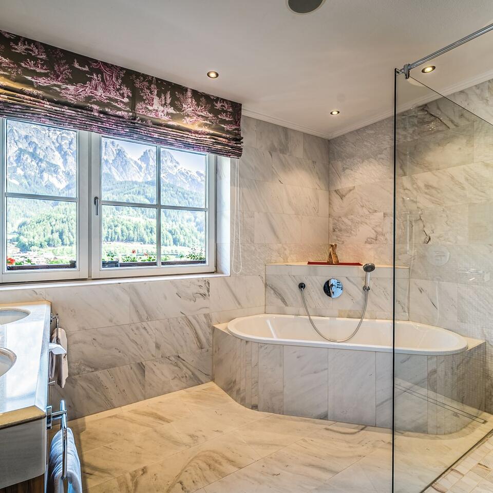 Modernes Badezimmer mit Marmor, Badewanne, Dusche und Fenster mit Bergblick