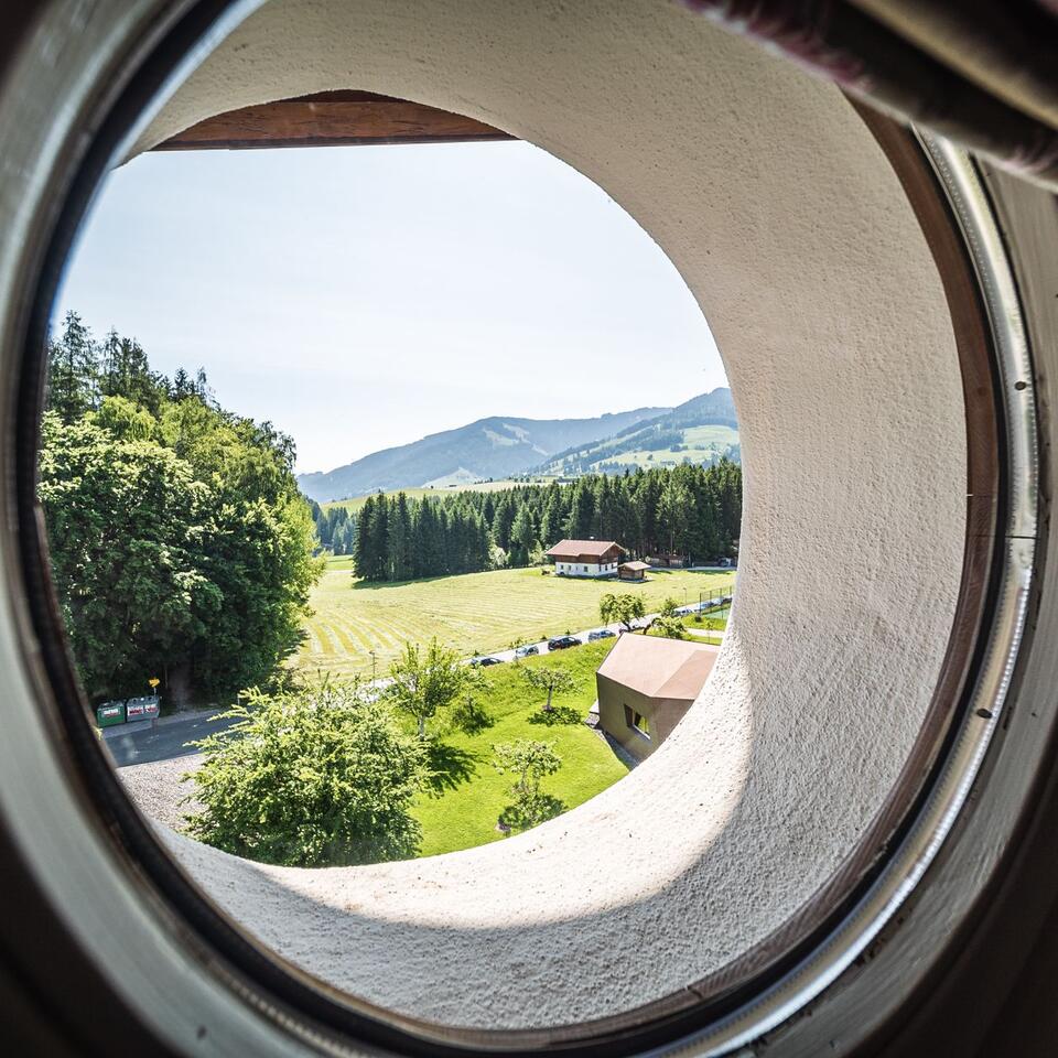 Blick durch rundes Fenster auf grüne Landschaft mit Wald und Häusern