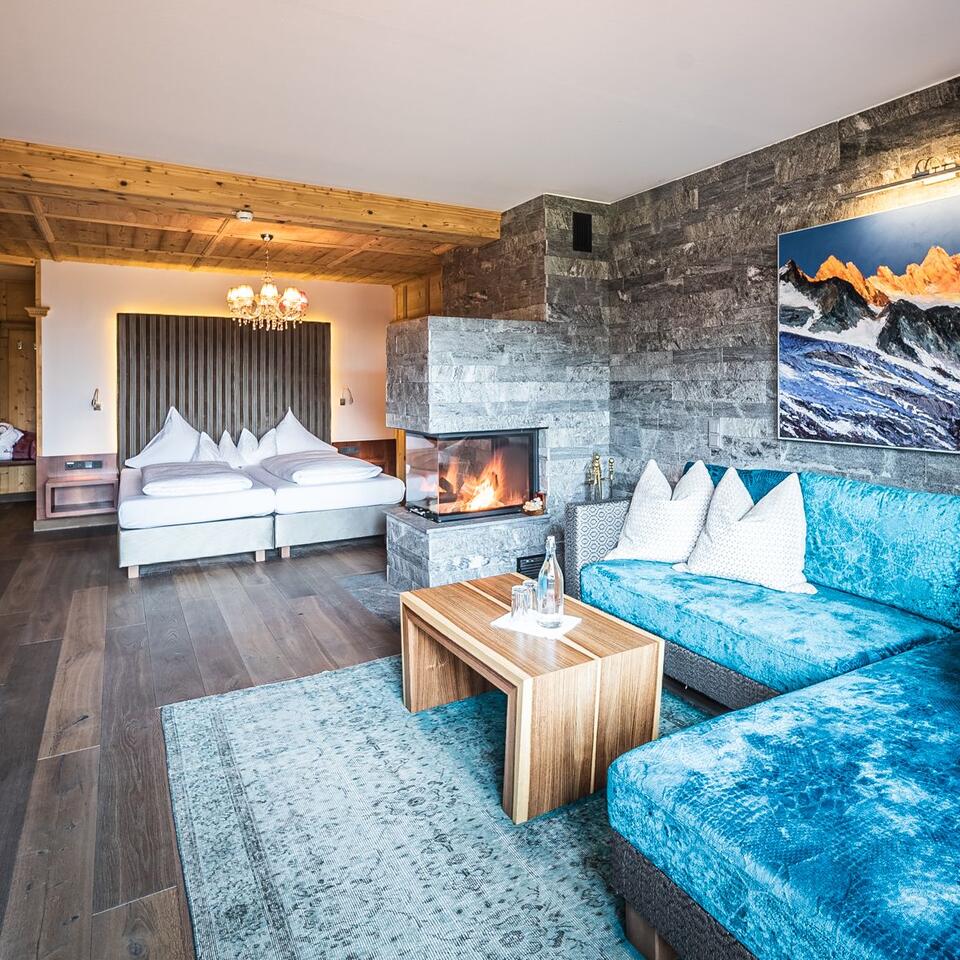 Hotelzimmer mit Kamin, blauem Sofa, Bett und Holzboden