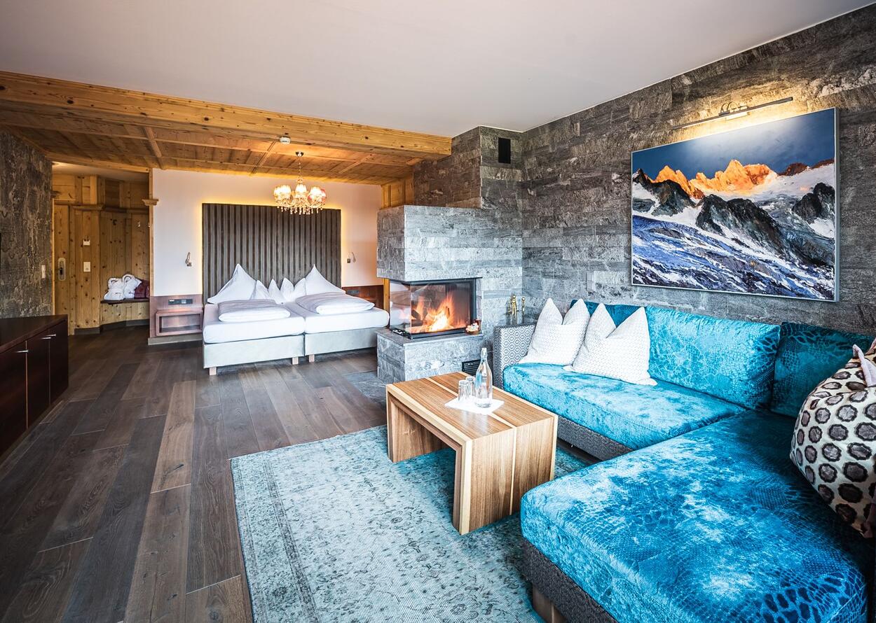 Hotelzimmer mit Kamin, blauem Sofa, Bett und Holzboden