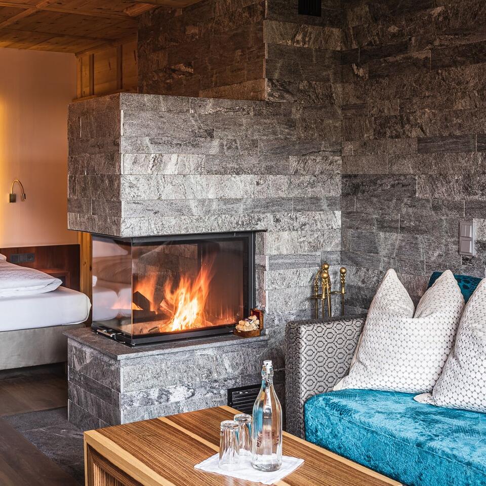 Kamin aus Stein mit brennendem Feuer, Sofa, Holztisch und Bett im Hintergrund