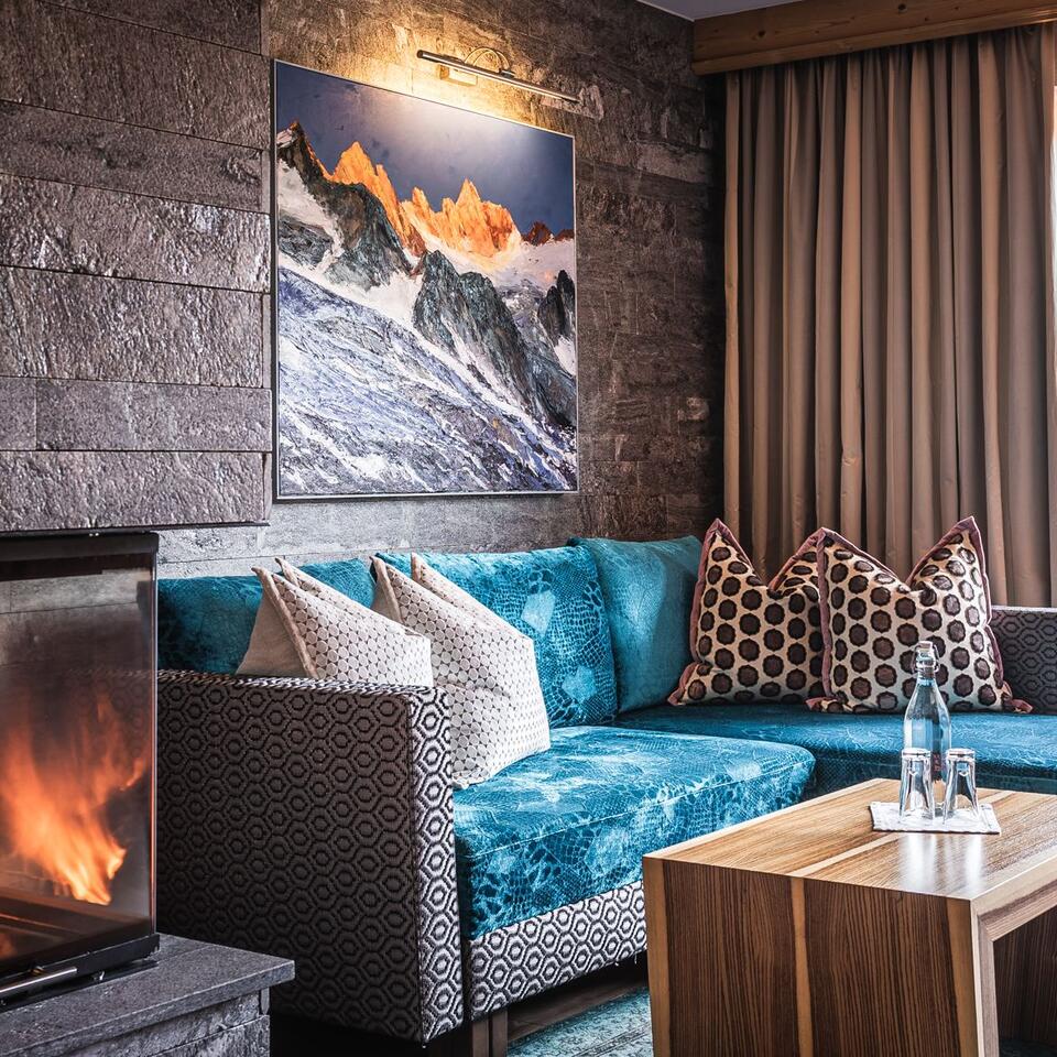 Gemütliches Wohnzimmer mit Kamin, türkisfarbenem Sofa und Berglandschaft-Bild an der Steinwand