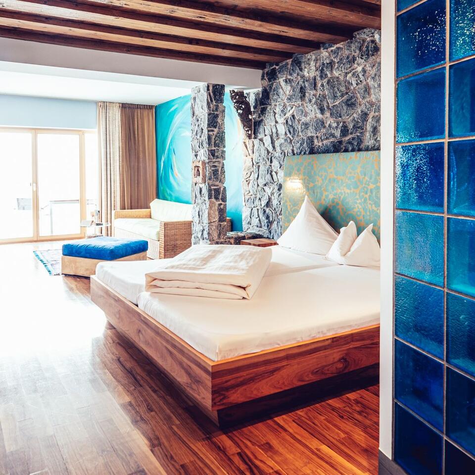 Schlafzimmer mit Doppelbett, Holzboden, Steinwand und blauen Akzenten