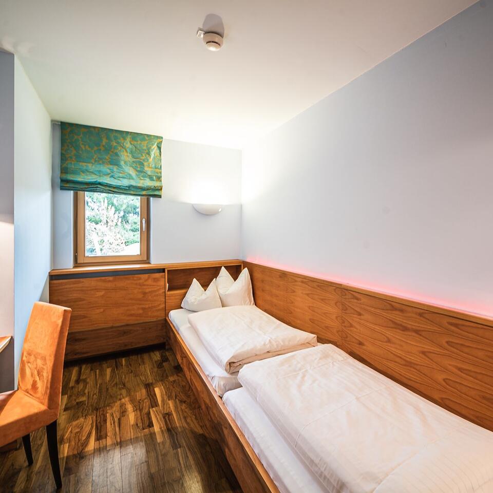 Schlafzimmer mit zwei Einzelbetten, Holzvertäfelung und Fenster mit grünem Rollo