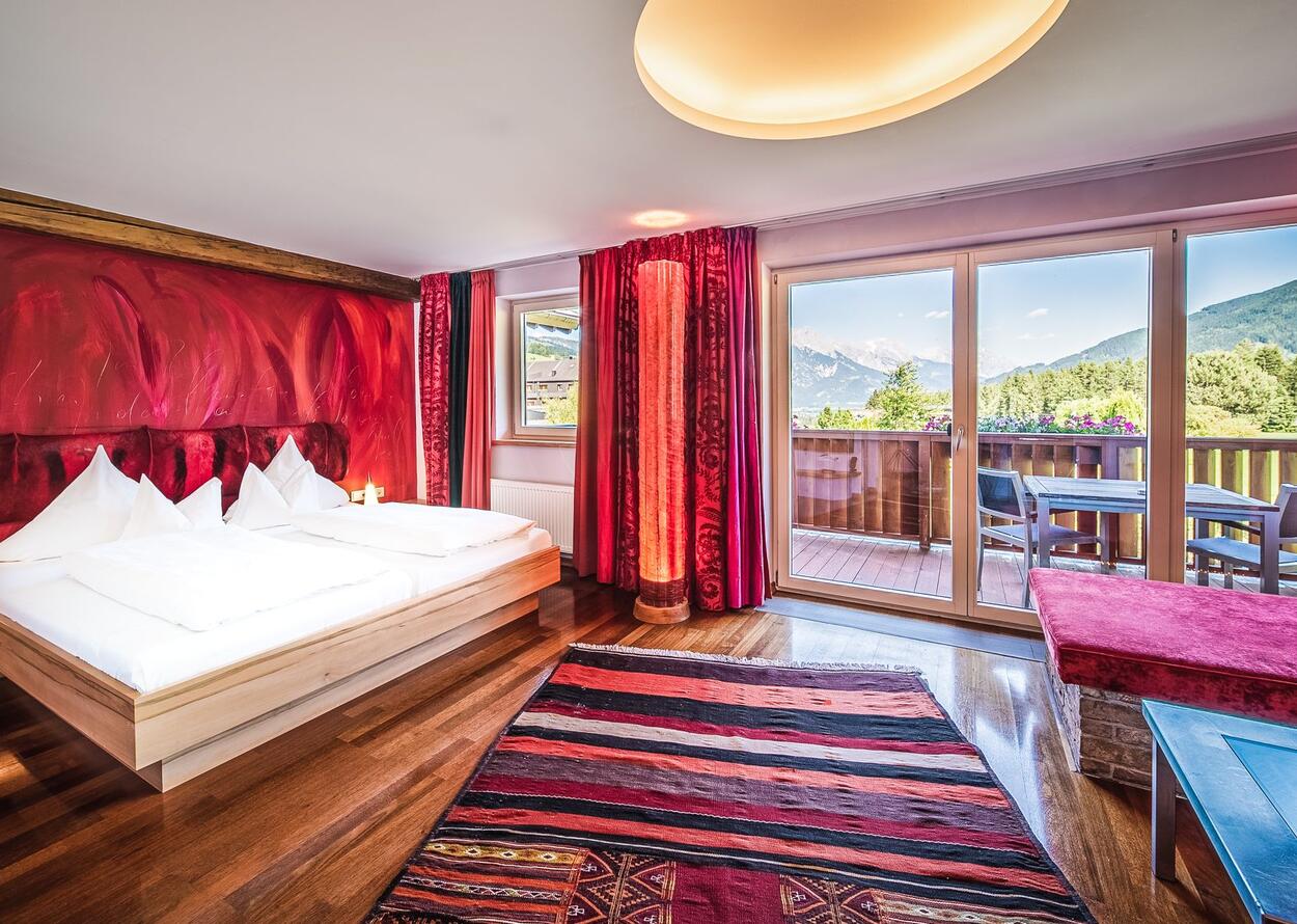 Schlafzimmer mit roter Wand, Teppich und Balkon mit Bergblick