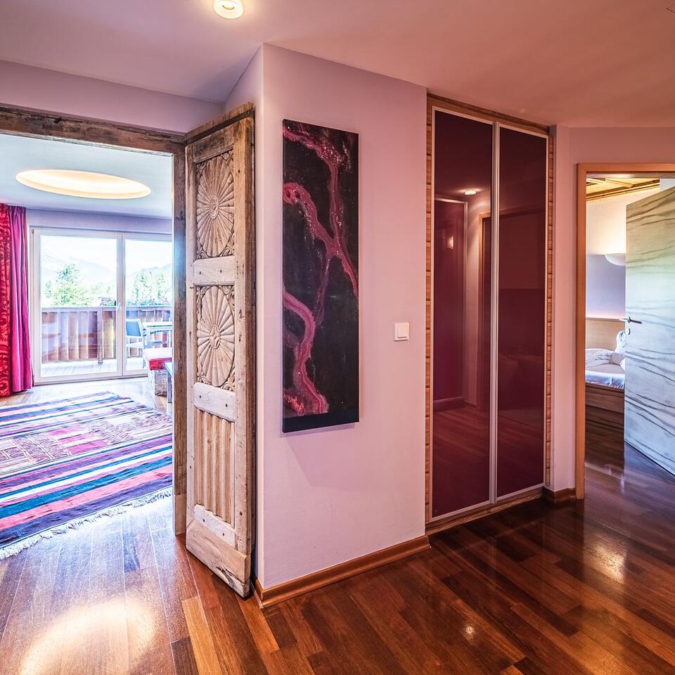Hallway with wooden floor, ornate wooden door, red art, sliding doors and view into room