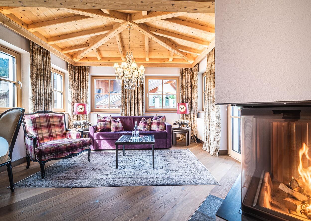 Gemütliches Wohnzimmer mit Holzbalkendecke, Kamin und lila Sofa