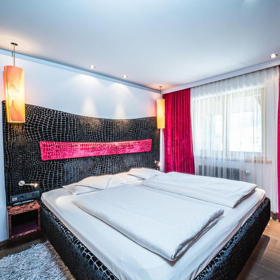 Bedroom with double bed, patterned headboard and red curtains