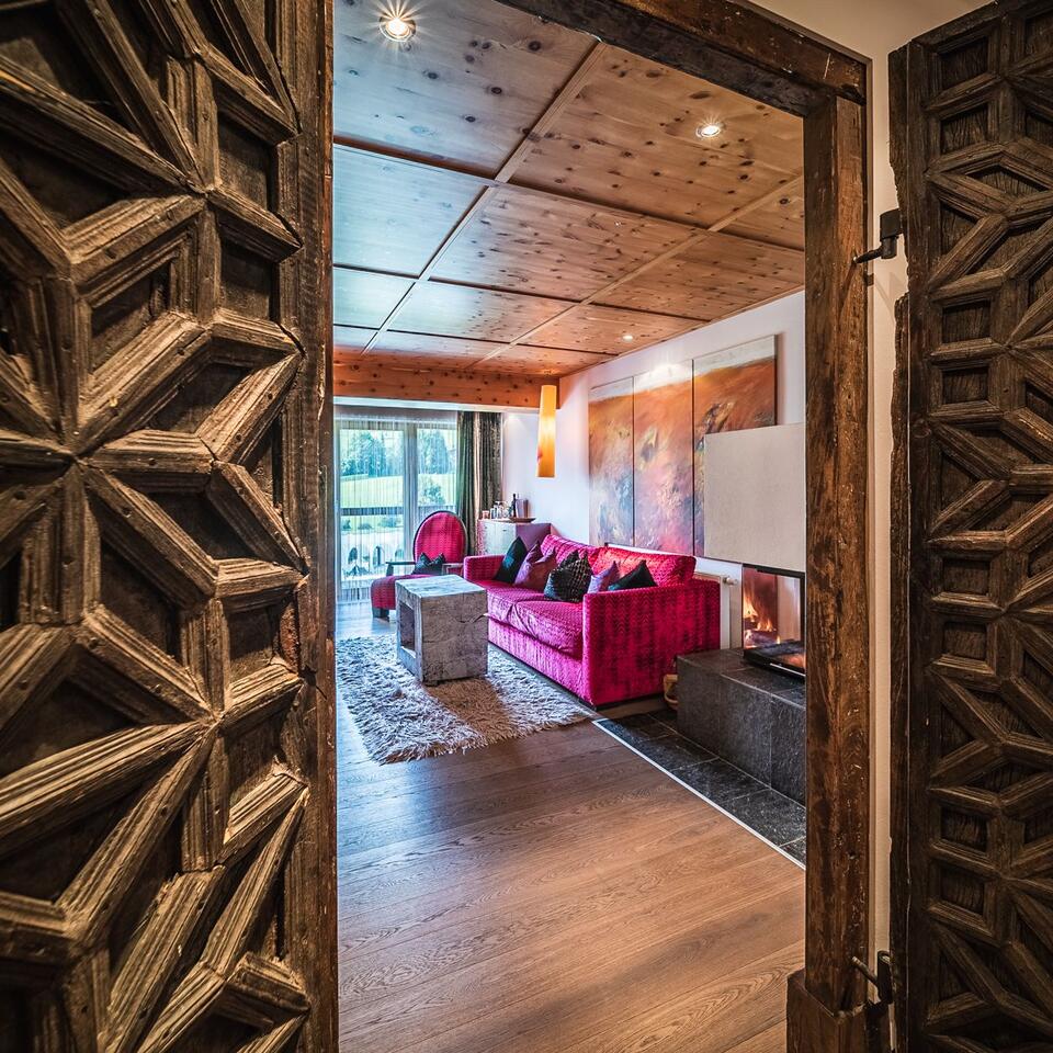 View through carved wooden door to living room with pink sofa and wooden ceiling