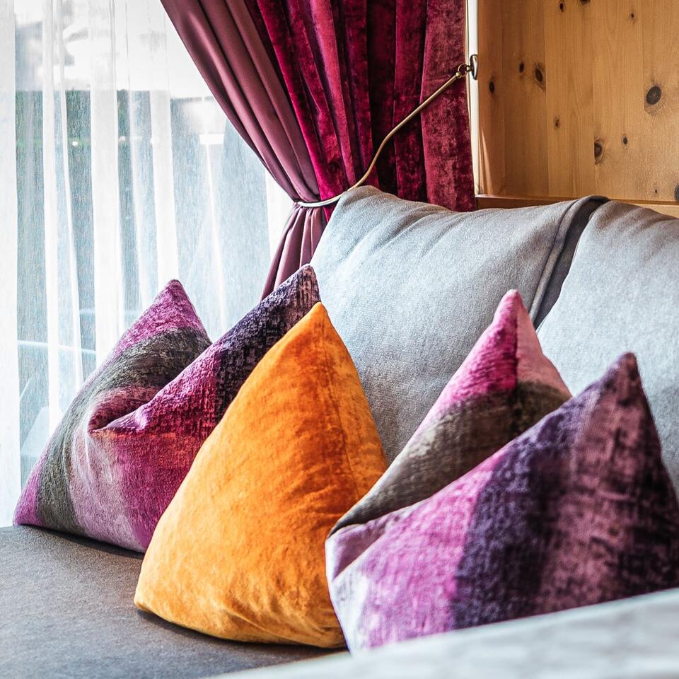 Pillows in different colors and textures on a couch in front of a curtained window