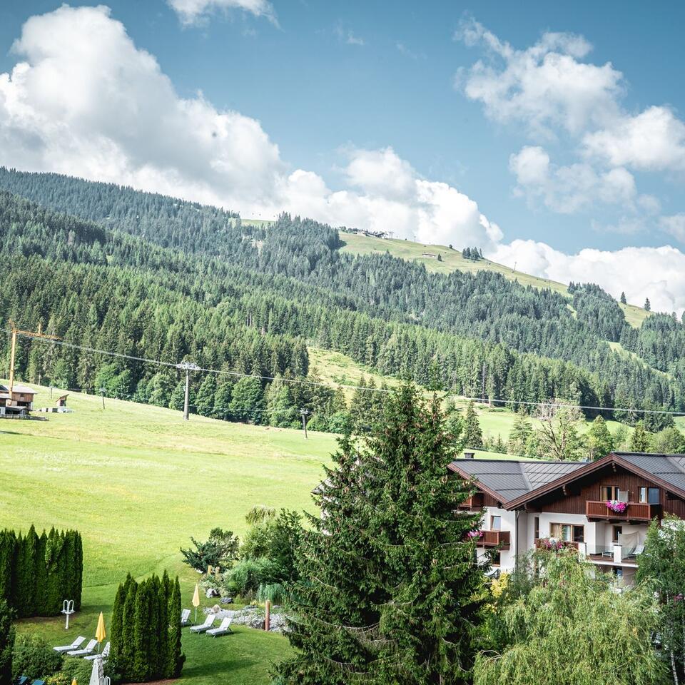 Hotel complex in front of a green mountain landscape with forest and blue sky