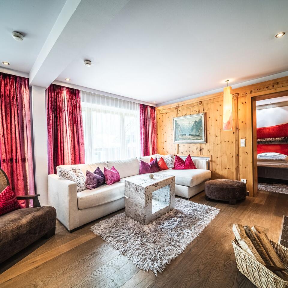 Wohnzimmer mit weißer Couch, Holzwand, roter Deko und Blick in ein Schlafzimmer