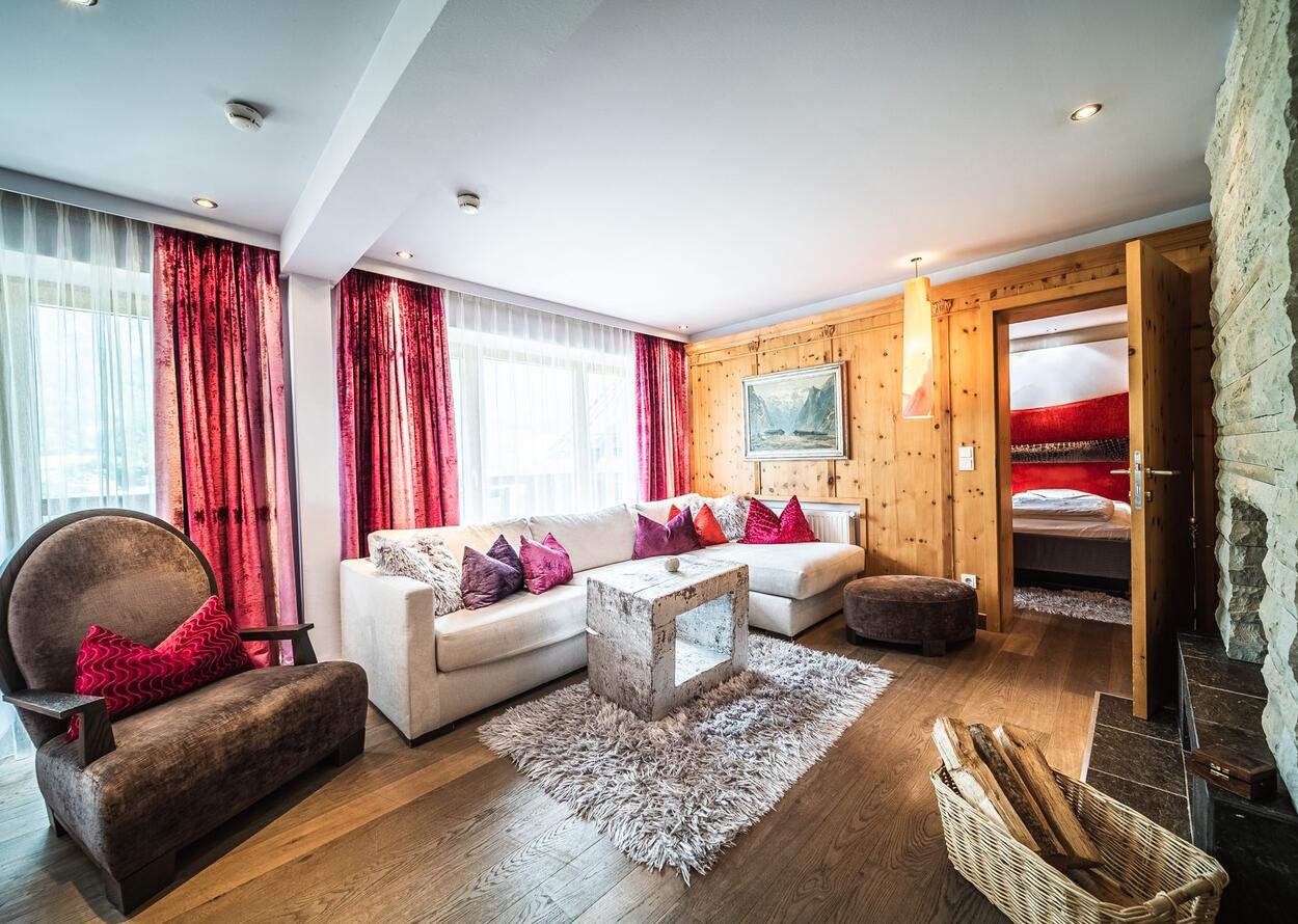 Wohnzimmer mit weißer Couch, Holzwand, roter Deko und Blick in ein Schlafzimmer
