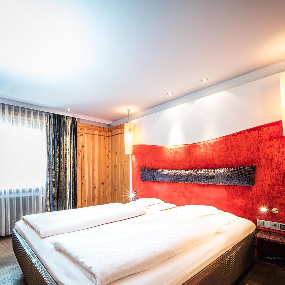Schlafzimmer mit Doppelbett, roter Wand, Holzvertäfelung und Vorhängen